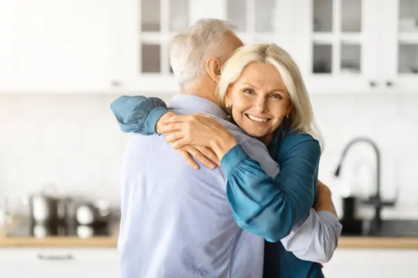 Portrait Of Romantic Older Spouses Hugging In Kitchen Interior, Loving Senior Man And Woman Having Fun Together At Home, Bonding And Smiling, Beautiful Elderly Woman Looking At Camera, Free Space