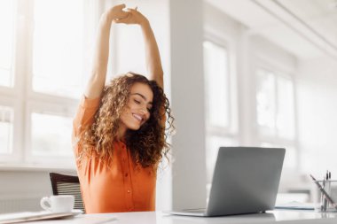 Neşeli iş kadını, kapalı gözleri ve bir gülümseme ile, çalışma alanında bir dizüstü bilgisayarla, parlak modern ofis ortamında, uzayı kopyalamak için ara veriyor.