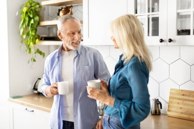 Mutlu yaşlı çift mutfakta sabah kahvesi içiyor, kıdemli adam ve kadın gülümsüyor, sohbet ediyor ve evde birlikte vakit geçiriyorlar, neşeli yaşlı eşler emeklilik keyfi yapıyor, yakın çekim yapıyorlar.
