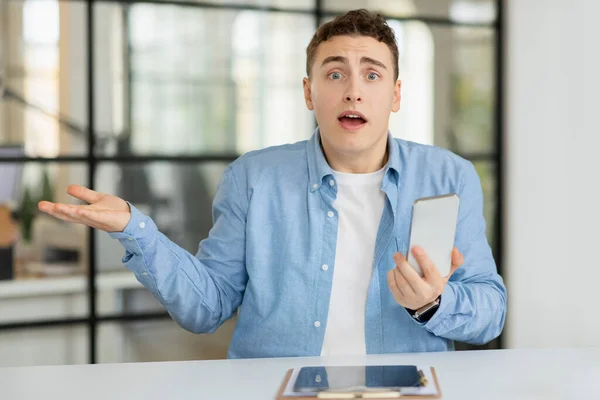 Shocked confused sad millennial european guy manager hold on hand free space and phone, suffer from mistake, problems at table in coworking office. Stress at work, business, bad job, newcomer