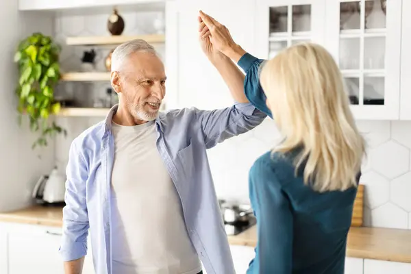 Portrait Of Active Senior Couple Dancing Together At Home, Romantic Elderly Man And Woman Holding Hands And Having Fun, Relaxing In Kitchen Interior, Enjoying Time With Each Other, Closeup
