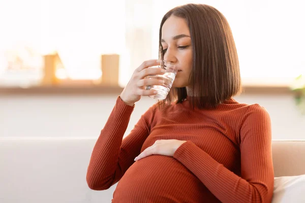 怀孕少女喝水 享受健康的液体 保证孕期的水份 坐在现代客厅的沙发上 — 图库照片
