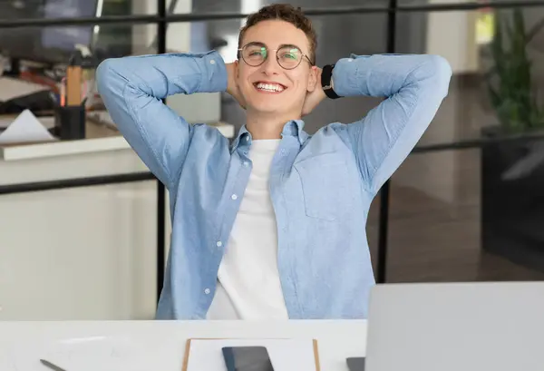 Satisfied handsome millennial caucasian guy manager in glasses with laptop rest at table in modern coworking office. Work with gadget, business break, success and relax at free time