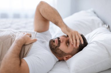 Adam yatakta baş ağrısından muzdarip, yatak odasında yatarken alnına dokunuyor. Orta yaşlı sakallı adam kendini kötü hissederek uyuyamıyor. Hipertansiyon ya da uykusuzluk sorunu