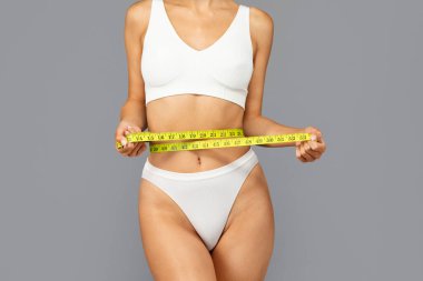 Beyaz spor giyimli genç Avrupalı bayanın gövdesinde gelişim ve sağlığı vurgulamak için belinde sarı bir şerit bulunur. Fitness ölçümü ve sağlık denetimi