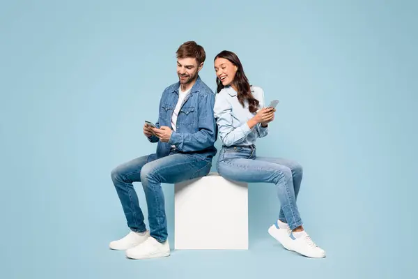 Zaręczona Para Dżinsowym Stroju Ciesząca Się Smartfonami Siedząc Tyłem Siebie — Zdjęcie stockowe