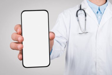 Laboratuvar önlüklü bir erkek doktor boş ekranlı bir akıllı telefonu sunuyor. Sağlık uygulamalarını veya hasta iletişim araçlarını sergilemek için ideal.