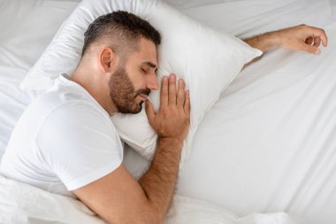 Orta yaşlı, beyaz sakallı bir adam rahat bir yatakta uzanıyor. İçerde huzur içinde kestiriyor. Uyuyan adam yatak odasında uyurken yastığa sarılıyor. Sağlıklı dinlenme
