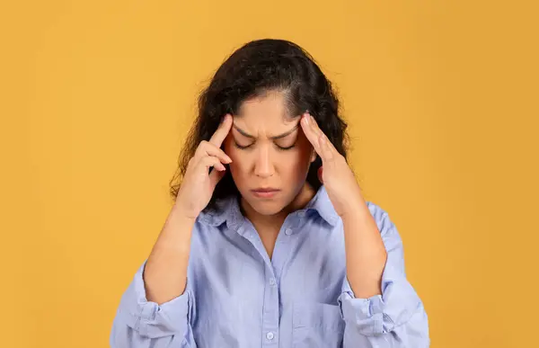 垂头丧气的拉丁裔年轻女子用手按摩庙宇 在黄色背景下患头痛 压力或疼痛 过度工作和保健问题 偏头痛 — 图库照片