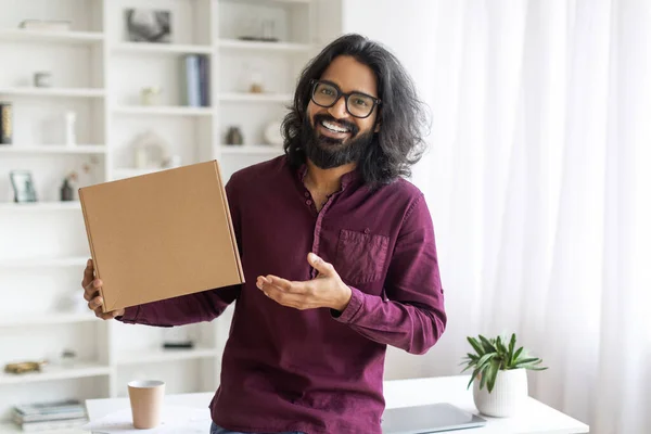Joyful Young Indian Man Holding Big Cardboard Box At Home, Happy Excited Eastern Guy Pointing At Delivered Parcel, Enjoying To Fast Shipping, Millennial Male Smiling At Camera, Copy Space