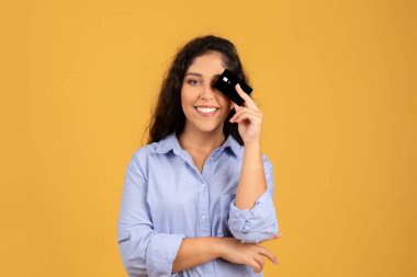 Milenyum esmer bayanın gündelik kredi kartı kullanması, eğlenmesi, satışta düşünmesi, turuncu stüdyo arka planında izole edilmesi. Finans rüyası, kâr, yeni alımlar için para