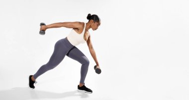 Vücut geliştirme. Beyaz Stüdyo Arkaplanındaki Güç Çalışması sırasında Afrika kökenli Amerikalı Fitness Kadını Dambıllarla Egzersiz Kas Kasları Ağırlık Tutma Ağırlığı. Boş Alanı Olan Panorama