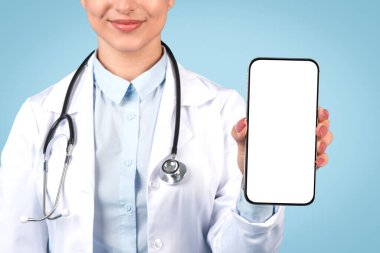 Laboratuvar önlüklü, sağIık uygulaması tanıtımı ya da hasta bilgileri için boş ekranlı akıllı telefonu gösteren kendine güvenen bir tıp uzmanı kadın.