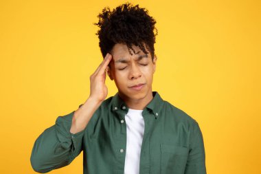 Bin yıllık mutsuz, gözleri kapalı, başı ağrıyan, başı ağrıyan, migreni olan, sarı stüdyo arka planında izole edilmiş, tapınak ovalayan siyah bir adam.