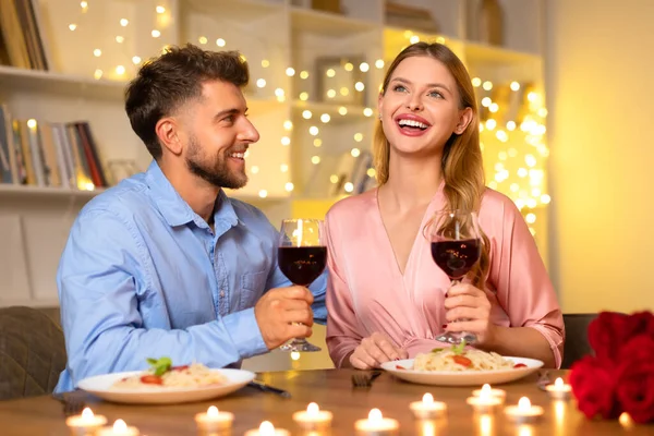 パスタとワインでロマンチックなディナーを楽しんでいる笑顔の男女 暖かい光り輝くライト 自由なスペースを背景にグラスを味わう — ストック写真
