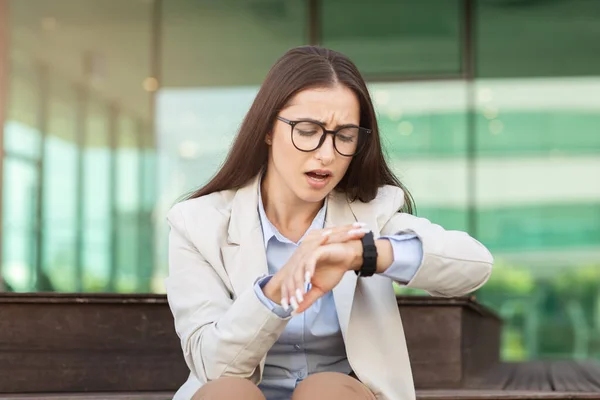 Sad stressed businesswoman checks watch with concerned expression, depicting urgency and the pressure of time management. Stress and time constraints in professional settings, late