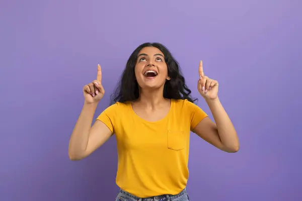 兴奋的 情绪激动的 漂亮的印度年轻女人 望着头顶上方的复制空间 展示出令人惊奇的广告和紫色的背景 — 图库照片