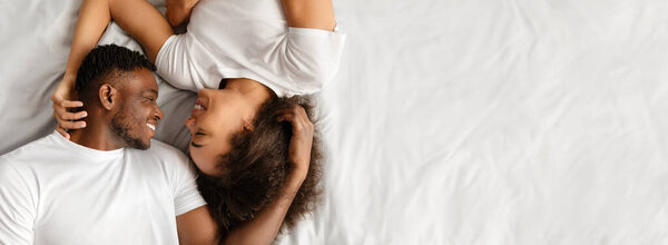 Above View Of Loving African American Couple Lying In Bed Having Intimate Moment Together In Bedroom Indoors. Lovers Smiling To Each Other Hugging Tenderly. Panorama, Free Space