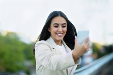 İspanyol iş kadını şehir dışında yürürken video konferansına katılıyor. Mutlu başarılı girişimci kadın iş için uzaktan iletişim cihazını kullanıyor.