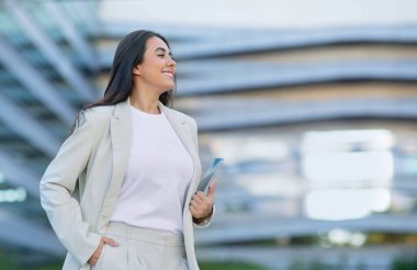 Modern ofis merkezinin yanındaki şehir caddesinde kendine güvenen İspanyol iş kadını akıllı telefonunu tutuyor ve mesaj için boş yere bakıyor. Kariyer ve teknolojide başarı