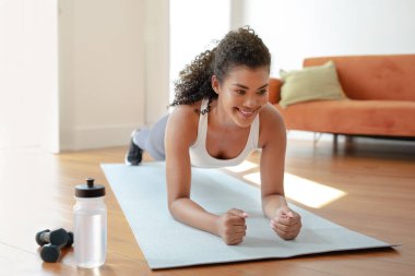 Gülümseyen sporcu kadın spor yapıyor evde spor paspası üzerinde dirsek egzersizi yapıyor sağlıklı kilo kaybı ve spor rutininin tadını çıkarıyor. Atletik vücut konsepti için fiziksel egzersiz. Spor motivasyonu