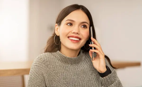Closeup of cheerful pretty young woman talking on phone at home. Happy brunette lady have conversation, using mobile phone, call with boyfriend, looking at copy space. Communication