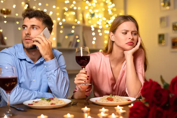 彼の日付を無視して電話をかけた男は ワインとパスタでロマンチックなディナーの間に退屈で失望した女性を残し 雰囲気が台無しにしました — ストック写真