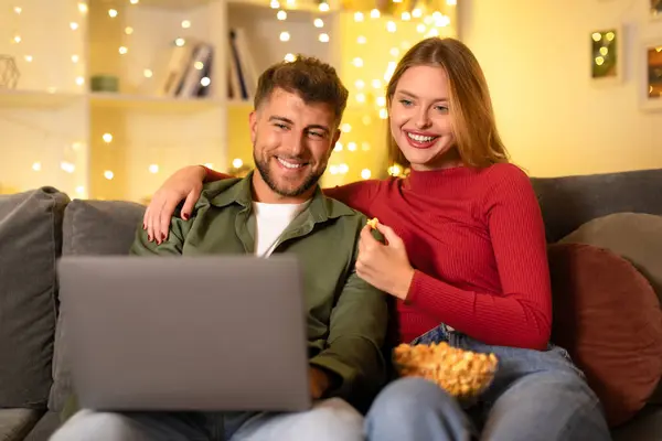 Relaxed Smiling Young Couple Sharing Popcorn While Browsing Laptop Seated — Stock Photo, Image