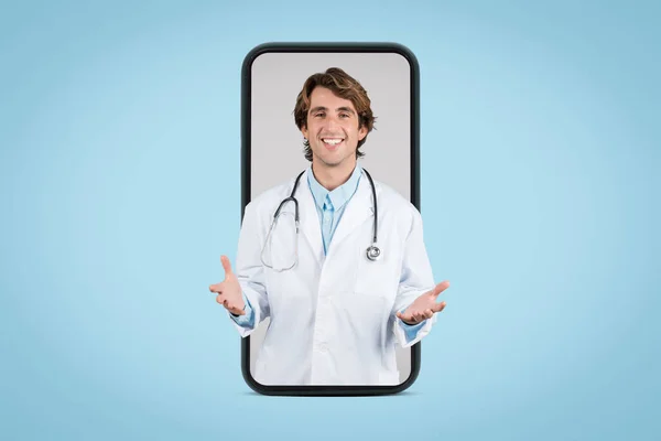stock image Virtual mental health support. Friendly male doctor in white medical coat having online appointment with patient, posing in huge smartphone screen, blue studio background