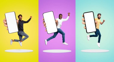 Joyful Young Men Jumping With Big Blank Smartphone In Hands Above Platforms Over Colorful Studio Background, Happy Excited Multiethnic Guys Demonstrating Empty Cellphone For Mobile Design, Mockup