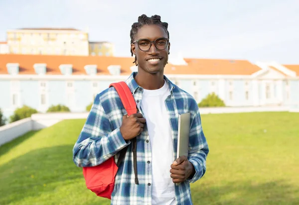 Friendly Black Student Guy Backpack Holding Closed Laptop Standing Backdrop — Zdjęcie stockowe