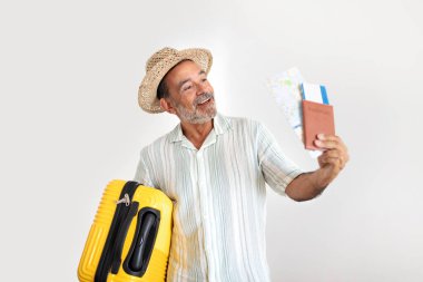 Senior Globetrotter. Happy Mature Man With Yellow Travel Suitcase Showing Passport With Boarding Pass Tickets, Happy About Great Vacation Tour Offer, Standing Against Gray Studio Wall