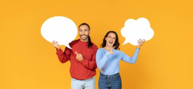 Smiling young european couple joyfully display empty thought bubbles, inviting ideas, sharing opinions, have conversation, chatting, against a sunny yellow backdrop, panorama