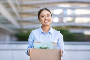 Japanese entrepreneur woman in city setting, happily carrying belongings box outdoor, symbolizing fresh start or new path in corporate world, seeking opportunities, career change and freedom