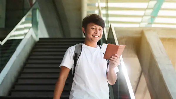 Happy young asian guy tourist going down stairs at airport or train station, checking his tickets, carrying backpack, holding passport, chinese man going vacation, travelling abroad