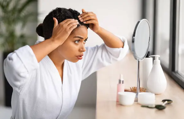 Dandruff Problem. Upset Black Woman Looking To Mirror At Her Hair Roots, Frustrated Young African American Female Wearing Bathrobe Suffering Dry Flaky Scalp, Making Beauty Routine At Home, Closeup