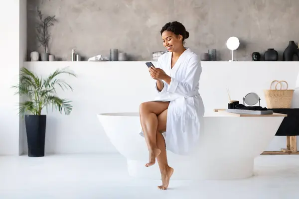 Happy Black Female Using Smartphone While Sitting Bathtub Bathroom Young — Foto de Stock