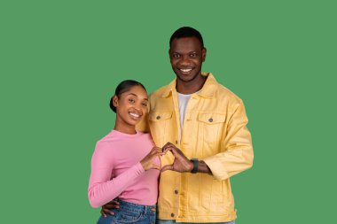 Cute loving african american couple embracing and showing heart symbol, matching fingers together, posing isolated on green studio background. Love, affectionate, relationships