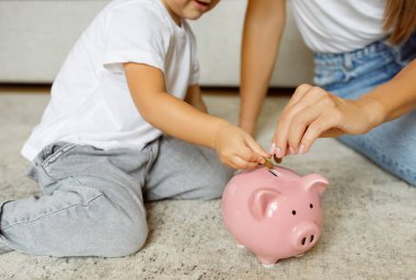 Family Savings. Mother And Little Daughter Inserting Coins To Piggy Bank At Home, Caring Mom Teaching Her Daughter How To Save Money, Sitting On Floor In Living Room, Cropped Shot, Closeup