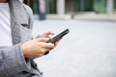 Unrecognizable businesswoman using smartphone, typing on device outdoors in urban setting. Modern communication and mobile technology. Copy space, cropped shot of lady texting on cell phone