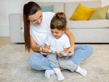 Mother And Little Daughter Checking New Toy While Playing Together At Home, Happy Young Mom And Cute Toddler Female Child Unpacking Colorful Blocks Set, Having Fun In Living Room Interior