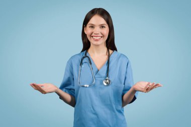 Young woman nurse in blue coat gesturing at the camera, engaging in online consultation against seamless blue background, digital healthcare