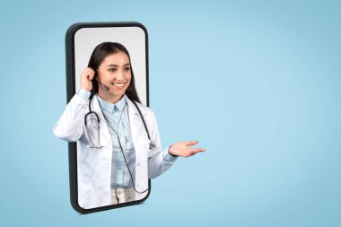 Female doctor with headset interacting through smartphone screen, exemplifying virtual consultation service on clear blue background, free space