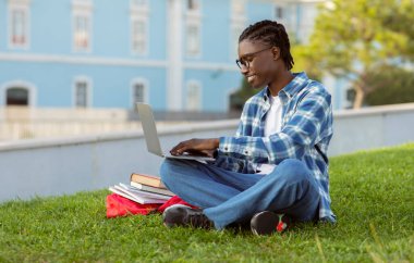 Happy black student guy typing on laptop having online lecture at university park, using computer to take notes and browse academic websites, enjoying e-learning and college education outside