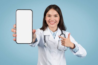 Enthusiastic female doctor presenting pointing at blank smartphone screen, perfect for illustrating e-health services and apps, blue background
