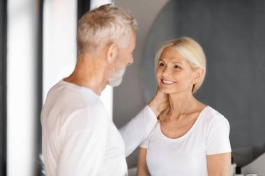 Romantic elderly couple sharing tender moment with gentle touches and loving gazes in serene bathroom setting, happy senior husband and wife exuding warmth and lifelong affection, closeup