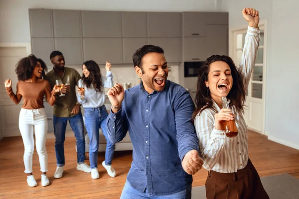 Energetic multicultural friends singing and dancing with joy in modern kitchen, having fun on students party as they celebrate with drinks, capturing essence of youthful weekends. Selective focus
