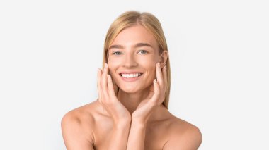 Avrupalı sarışın bayan kusursuz yüzlere dokunuyor nemlendirici kozmetik ürünler uyguluyor, doğal güzellik kavramı ve mükemmel cilt bakımı, beyaz stüdyo arkaplanı, panorama