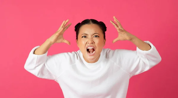 身穿白色运动衫 怒气冲冲的年轻亚洲女人冲着相机尖叫 怒气冲冲地举起双手 表达负面情绪 在充满活力的粉色工作室背景下孤立无援 — 图库照片