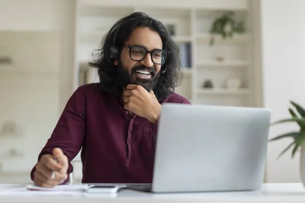 Remote Work. Smiling Indian Male Freelancer Working With Laptop At Home, Handsome Eastern Male Wearing Headset Looking At Computer Screen And Taking Notes, Enjoying Distant Job, Copy Space